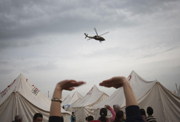 People wave at a military helicopter flying past at a stadium currently used as a relief shelter campsite for earthquake victims in Ercis Oct 26, 2011. Turkey struggles to shelter people after quake