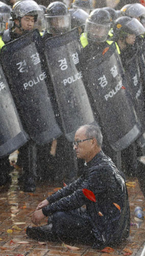 A protester sits in front of riot police as the police use water cannons to disperse a rally against the South Korea-US free trade agreement (FTA) talks in Seoul Nov 3, 2011. South Koreans protest free trade agreement with US